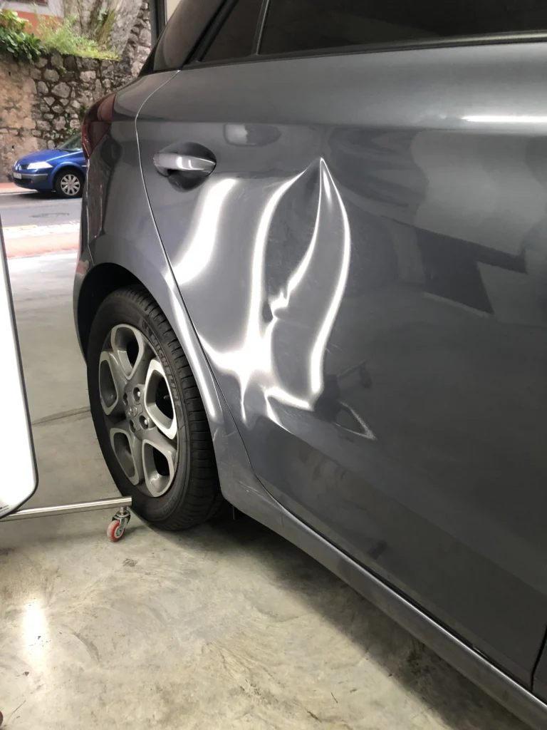 Varillero sacabollos trabajando en la chapa lateral de coche para eliminar abolladuras con método PDR