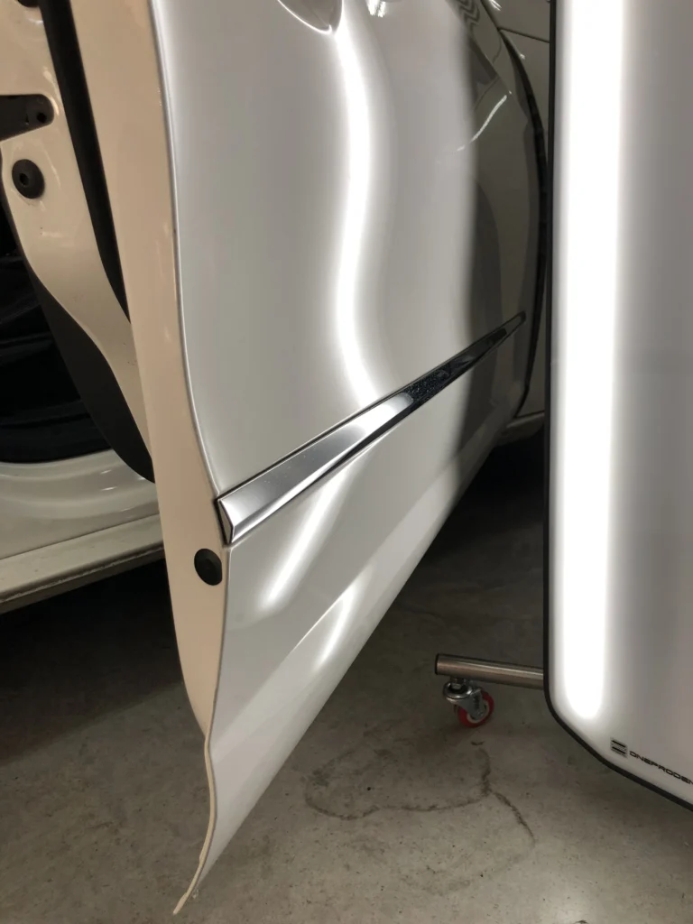 Varillero sacabollos reparando la chapa de la puerta del coche para eliminar abolladuras mediante método PDR profesional.