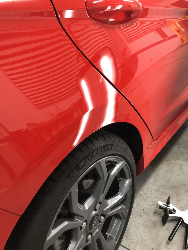 Varillero sacabollos trabajando en la chapa lateral de coche para eliminar abolladuras con método PDR